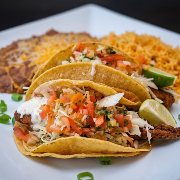 Three fish tacos with pico de gallo, shredded cabbage, and lime, served with rice and beans.