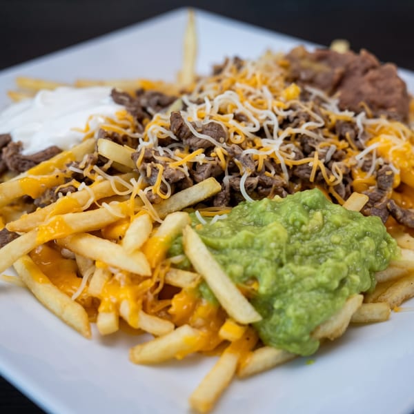 Loaded french fries with steak, cheese, guacamole, sour cream, and refried beans on a white plate.