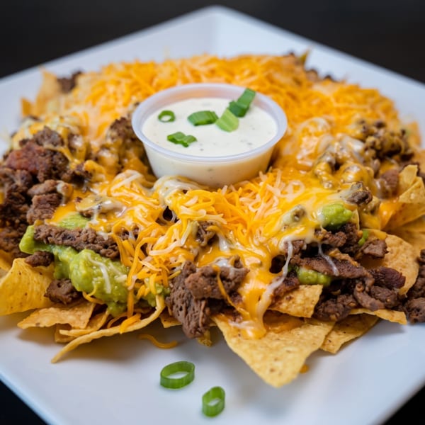 Loaded nachos with ground beef, guacamole, melted cheese, and a side of white sauce.