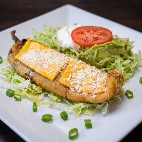 A chile relleno topped with cheese, served on lettuce with guacamole, sour cream, and tomato.
